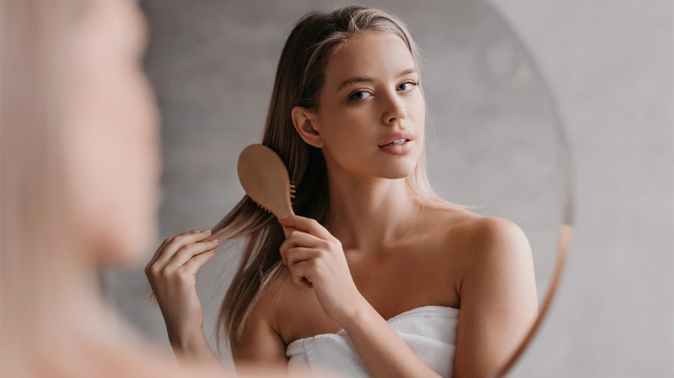 Portret kobiety czeszącej długie blond włosy w lustrze drewnianą szczotką