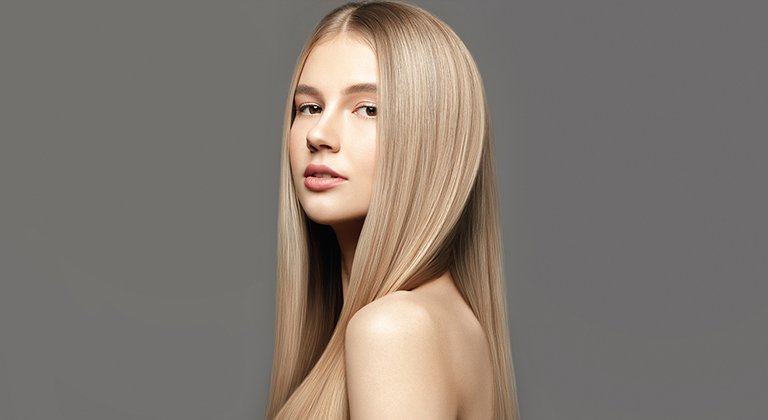 Młoda kobieta z prostymi blond włosami na szarym tle.