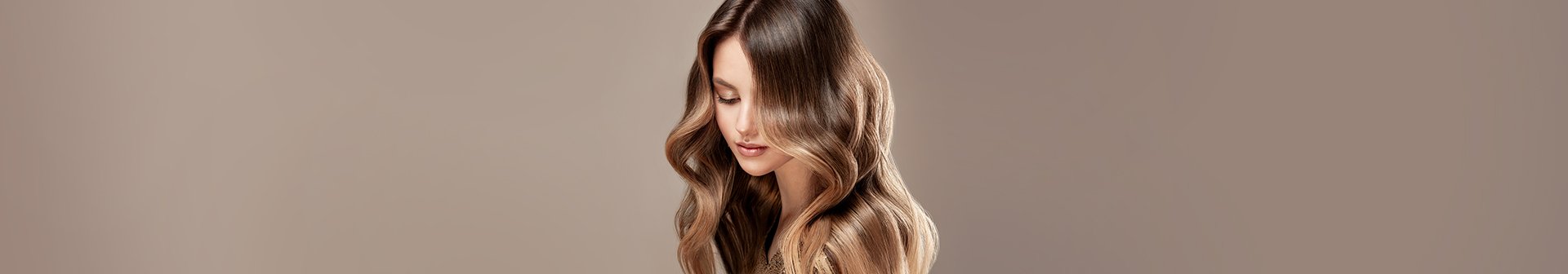 Piękna modelka z długimi, błyszczącymi i falowanymi włosami zaprezentowanymi po zabiegu koloryzacji z delikatnymi blond pasemkami.