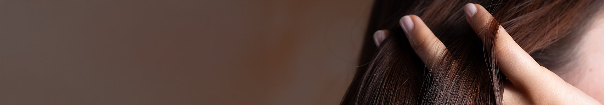 Zbliżenie na palce kobiety, która przeczesuje nimi ciemne brązowe włosy