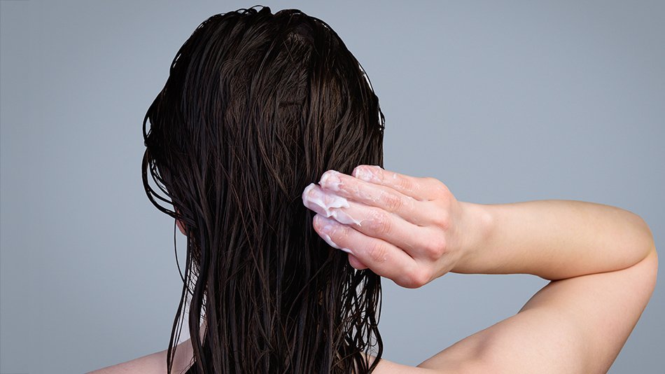 Kobieta pod prysznicem nakłada odżywkę na mokre włosy