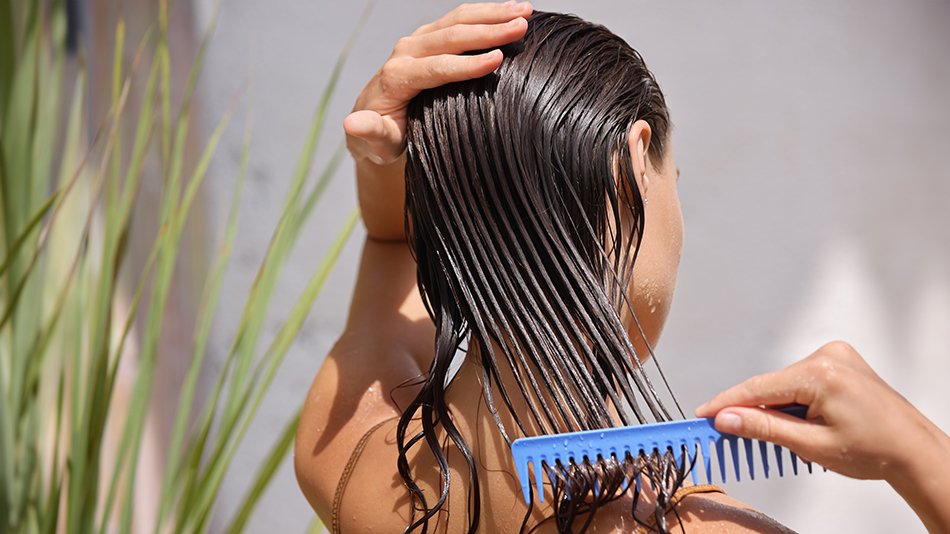 Kobieta rozczesuje włosy grzebieniem, by równomiernie rozprowadzić maskę na włosach