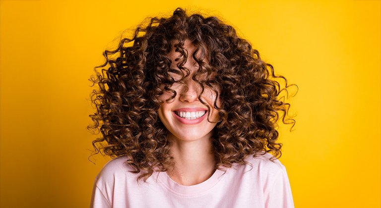 Śmiejąca się kobieta z mocno kręconymi włosami.