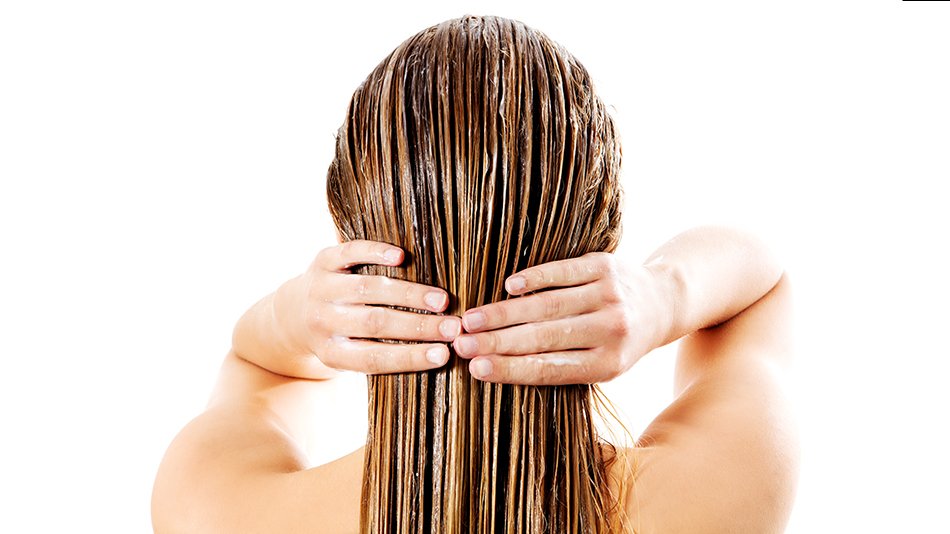 Młoda kobieta nakłada maskę na mokre włosy.