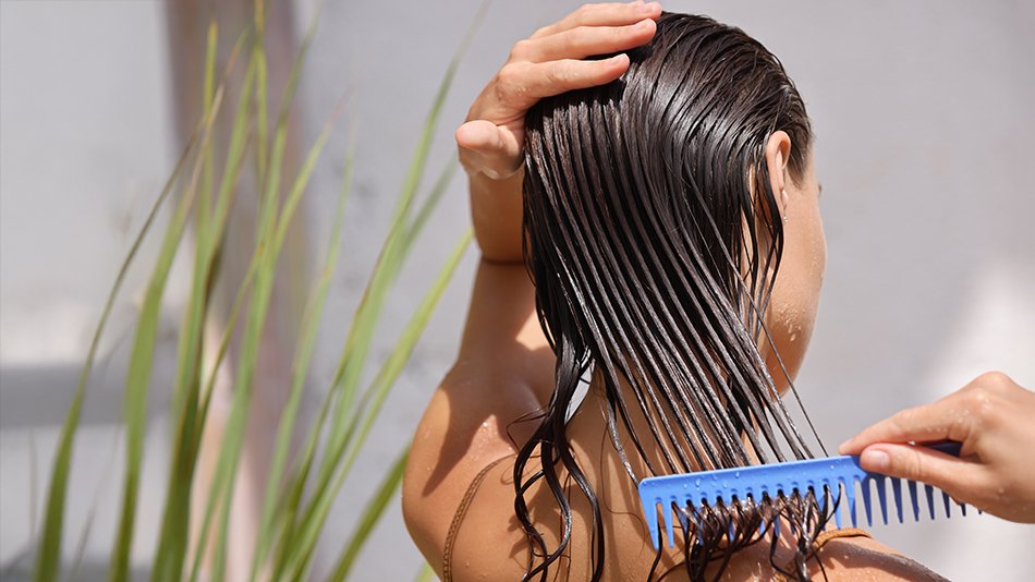 Kobieta pod prysznicem rozprowadza grzebieniem odżywkę na mokrych włosach