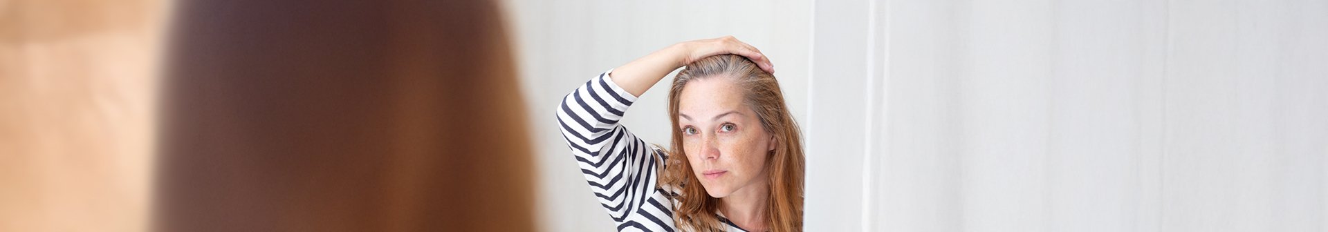 Młoda kobieta przeglądająca w lustrze pierwsze oznaki siwienia