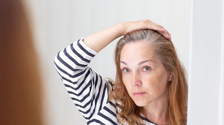 Młoda kobieta przeglądająca w lustrze pierwsze oznaki siwienia