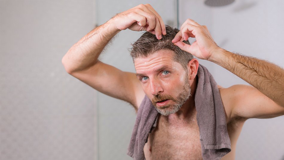Mężczyzna obserwujący w lustrze pierwsze siwe włosy