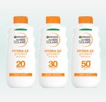 Trzy butelki mleczka Garnier Ambre Solaire Hydra 24h z pomarańczowymi kapslami, na jasnoniebieskim tle