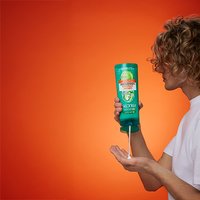 Zielona odżywka Garnier Fructis Grow Strong na żółtym stołku, obok osoba z mokrymi lokami
