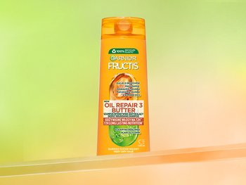 Pomarańczowa butelka szamponu Garnier Fructis na przezroczystej półce, na zielono-pomarańczowym tle