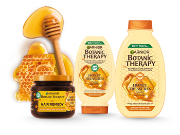 Trzy produkty Garnier Botanic Therapy Honey Treasures z łyżką do miodu i plastrem miodu, na białym tle