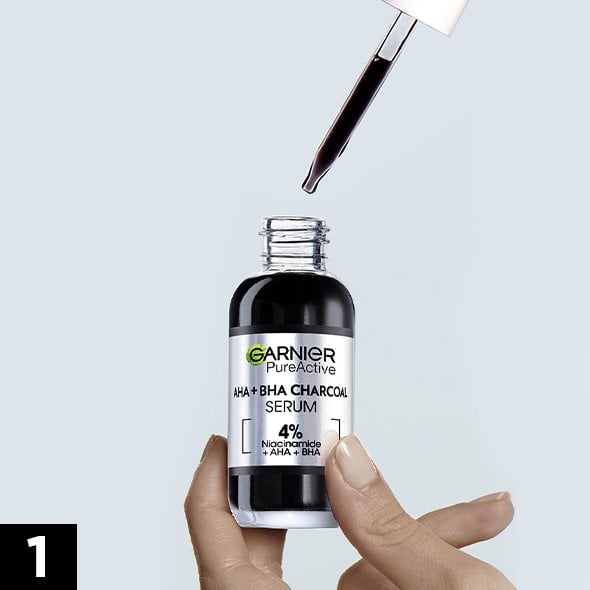Dłoń trzyma ciemną buteleczkę serum, pipeta z ciemnym płynem nad otworem