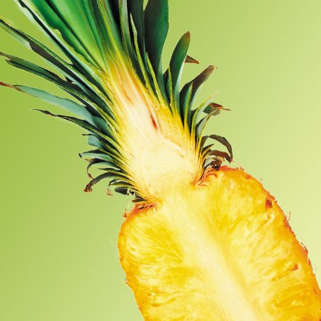 Ananas przekrojony wzdłuż, odsłaniający żółty miąższ i zieloną koronę, na jasnozielonym tle