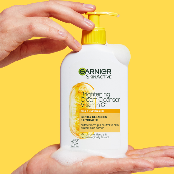 Rozświetlający krem myjący Garnier SkinActive z witaminą C, butelka z żółtą pompką trzymana w dłoniach