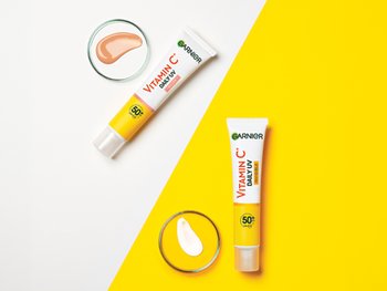 Dwie tubki Garnier Vitamin C Daily UV i dwa naczynka z próbkami w odcieniu skóry i bezbarwnym