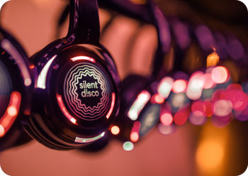 Czarna słuchawka świecąca na czerwono z logo „silent disco”, w tle kolorowe bokeh