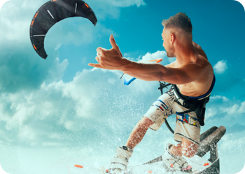 Mężczyzna kitesurfingowy pokazuje znak „shaka”, wyskakując z wody, na tle błękitnego nieba