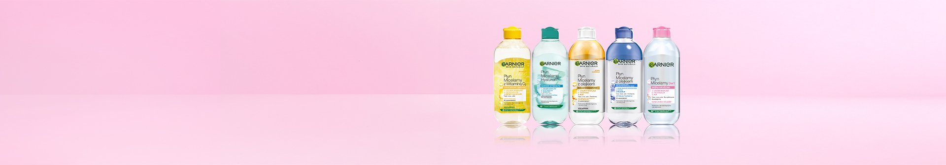 Pięć przezroczystych butelek płynu micelarnego Garnier w rzędzie z odbiciem, na jasnoróżowym tle