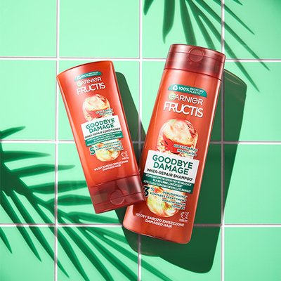 Dwie pomarańczowe butelki Garnier Fructis Goodbye Damage (szampon, odżywka) ukośnie, na miętowym tle