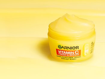 Jaskrawożółty, otwarty słoik kremu Garnier Vitamin C Fresh & Bright z porcją produktu, na żółtym tle