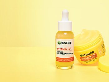 Dwa produkty Garnier z witaminą C: buteleczka z pipetą i przechylony żółty słoik kremu