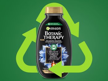 Czarna butelka szamponu Garnier Botanic Therapy ze złotym kapslem przed zieloną strzałką recyklingu