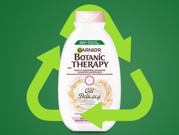 Biała butelka szamponu Garnier z różowym kapslem w dużym symbolu recyklingu, na ciemnozielonym tle