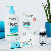 Cztery produkty Garnier PureActive na białym blacie, w tle niebieski ręcznik i roślina