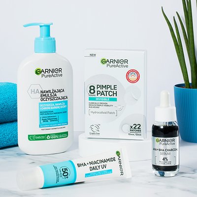 Cztery produkty Garnier PureActive na białym blacie, w tle niebieski ręcznik i roślina
