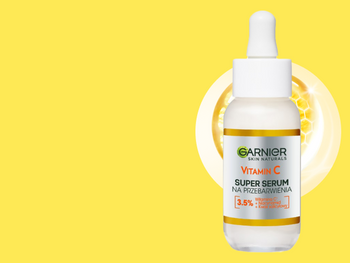 Biała buteleczka Garnier Vitamin C Super Serum z pipetą, na żółtym tle ze świecącym plastrem miodu