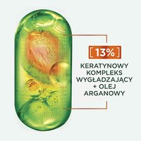 Przezroczysta zielona kapsułka z pomarańczowo-żółtymi kroplami płynu, na jasnoszarym tle
