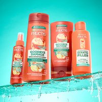 Cztery pomarańczowe butelki Garnier Fructis Goodbye Damage na mokrej powierzchni, na turkusowym tle