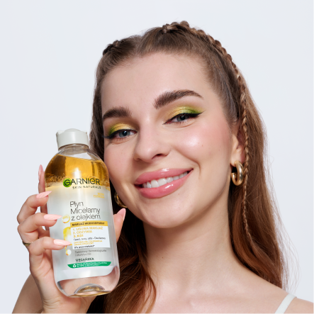 Uśmiechnięta kobieta prezentuje dwufazowy płyn micelarny Garnier, na białym tle Uśmiechnięta kobieta prezentuje dwufazowy płyn micelarny Garnier, na białym tle