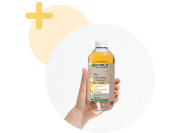 Szklana kolba ze złotym olejkiem oddzielającym się od płynu, obok butelka Garnier, na złotym tle