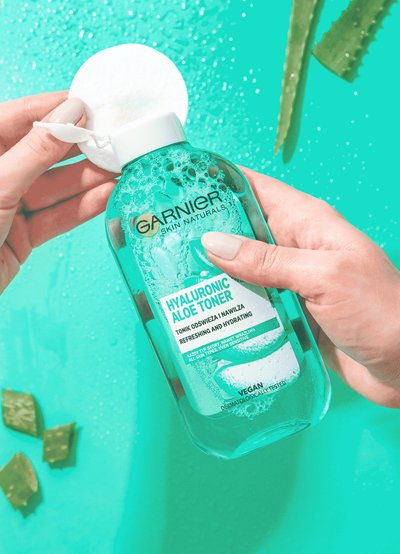 Dłonie trzymają butelkę toniku Garnier Skin Naturals Hyaluronic Aloe i płatek kosmetyczny