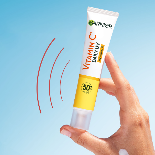 Dłoń trzyma żółto-białą tubkę filtra Garnier z białym produktem i czerwonymi liniami, na niebieskim tle