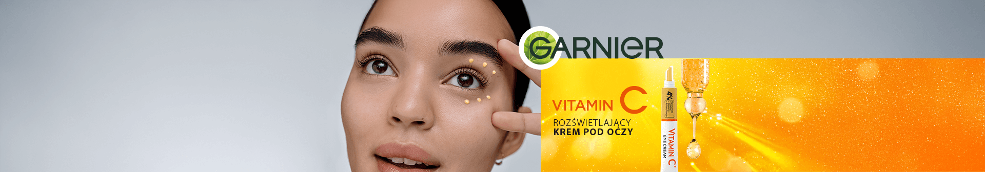 Kobieta nakłada kropki żółtego kremu pod oko, napis „Vitamin C rozświetlający krem pod oczy”